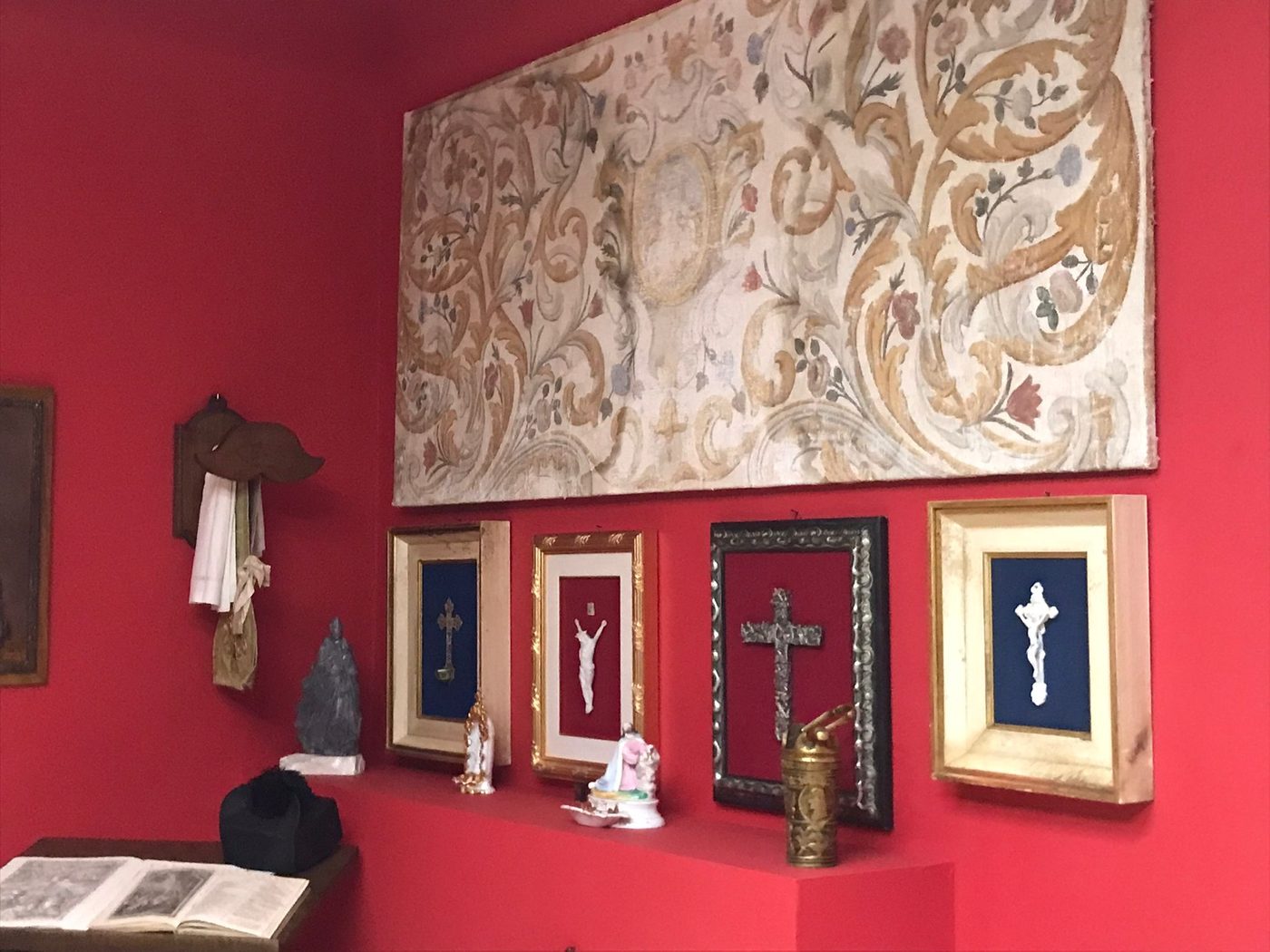 La parete rossa con crocifissi incorniciati e la quadreria
